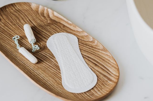 From above of cotton tampons and daily liner on wooden stand and toothbrushes and hand cleaner in jar and creams jars and perfume bottle placed on white marble surface near sink